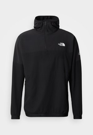 Mustast kergest materjalist lukuga pullover, millel on kõrge krae, pikad varrukad ja väike logo rinnal.