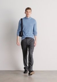 Ανοιχτό μπλε πουλόβερ με γιακά, εφαρμοστό, συνδυασμένο με σκούρες γκρι παντελόνες. Μαύρη τσάντα χιαστί, κομψά παπούτσια. Ουδέτερο φόντο.