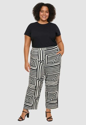 T-shirt nero a maniche corte abbinato a pantaloni a gamba larga e vita alta con una fantasia geometrica a righe bianche e nere. Tacchi neri con cinturini.