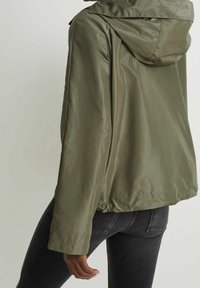 Veste légère vert olive avec capuche, texture lisse, ourlet élastique et coutures visibles à l'arrière.