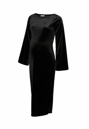 Robe de maternité en velours noir avec des manches longues, un décolleté bateau et une fente sur le côté, présentant un design ajusté pour accueillir un ventre qui s'arrondit.