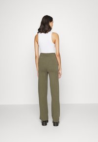 Calças de perna larga em verde-azeitona, feitas de um tecido macio. Apresentam uma cintura alta e um design liso e limpo, sem adornos visíveis.