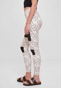 Tights med blomstermønster på en beige bakgrunn, med svarte aksenter og paneler. Kombinert med brune sandaler med stropper.