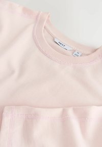 Chemise rose clair en coton à col rond et pantalon assorti, posés à plat, montrant le col côtelé et les coutures, avec l'étiquette de la marque « NEXT » visible en taille M.