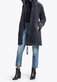 Vatteret marineblå kordfløjljakke med høj krave, sidelommer og ribbede manchetter, parret med lyseblå denimjeans og sorte ankelstøvler.