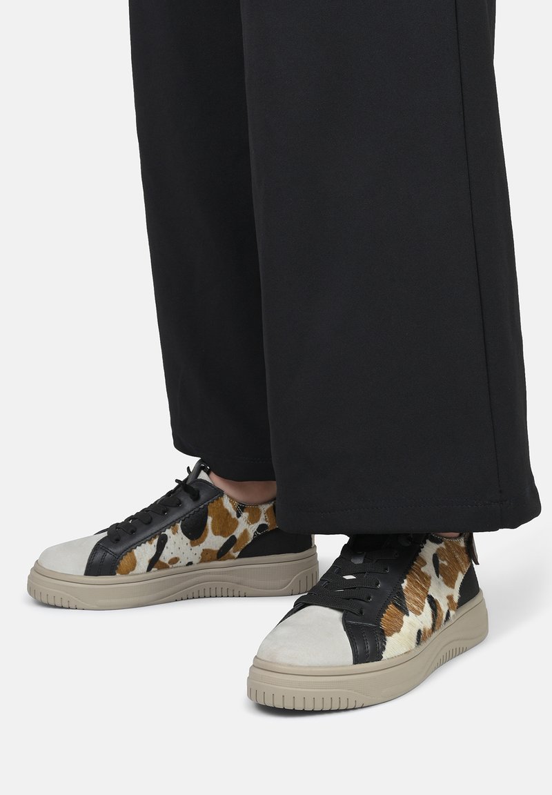 Sneaker in pelle e tessuto con un motivo maculato marrone e bianco, accenti neri e una suola beige testurizzata. Il design presenta lacci e un profilo basso.