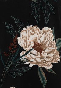 Květinová látka s velkými béžovými pivoňky a zelenými listy na černém pozadí, s texturovanými detaily v okvětních lístcích a listí.