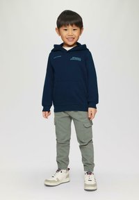 Marineblaue Kapuzenjacke mit einer Fronttasche und hellblauem grafischem Text, kombiniert mit olivgrünen Cargo-Hosen und weißen Sneakers mit grauen Akzenten.