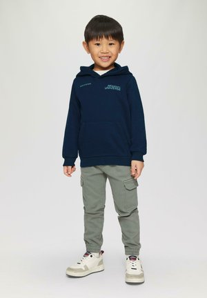 Hoodie bleu marine avec poche avant et texte graphique bleu clair, associé à un pantalon cargo vert olive et des baskets blanches avec des accents gris.