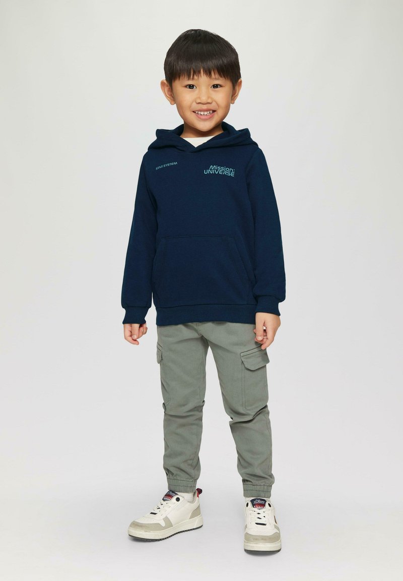 Marineblaue Kapuzenjacke mit einer Fronttasche und hellblauem grafischem Text, kombiniert mit olivgrünen Cargo-Hosen und weißen Sneakers mit grauen Akzenten.