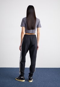 Sportig outfit bestående av en kortärmad grå t-shirt och svarta joggers med vita sidostreck, matchat med svarta sneakers och texturerat hår.