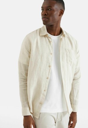 Lichtbeige linnen shirt met lange mouwen, knopen aan de voorkant en borstzak; heeft een ontspannen pasvorm en subtiele textuur.