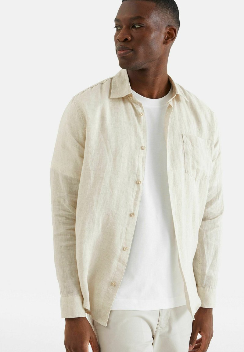 Lichtbeige linnen shirt met lange mouwen, knopen aan de voorkant en borstzak; heeft een ontspannen pasvorm en subtiele textuur.