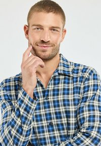 Chemise à carreaux bleue et blanche avec un col décontracté, présentant des motifs de carreaux contrastants et une texture douce.