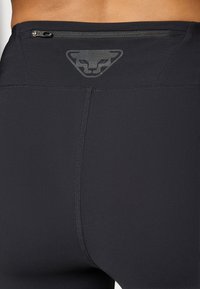 Juodos sportinės leggingai su lygia tekstūra, turinčios diskretišką užtrauktuko kišenę nugaros pusėje ir subtilų logotipą įspaustą šalia juosmens.
