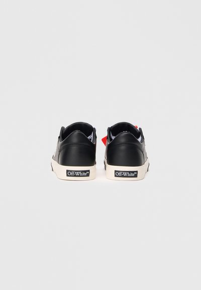 Sneaker in pelle nera con suola bianca, vista posteriore. Presenta accenti rossi e blu, etichetta del marchio e pannello in pelle testurizzata.