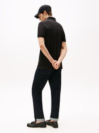 Svart polo skjorte, mørke jeans med oppbrettede ermer, svarte loafers. Enkel design, uformell estetikk, rene linjer og minimale mønstre.