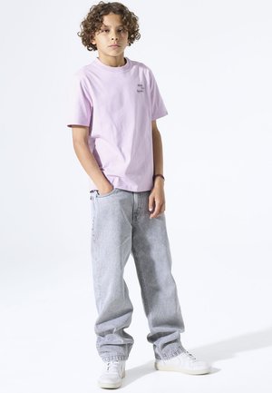 Lila katoenen T-shirt met korte mouwen en een klein logo, gecombineerd met lichtgrijze losse denim jeans en witte sneakers.