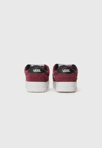 Vans sneakers in a burgundy suede finish, featuring a white rubber sole and black accents on the heel with logo detailing on the back.