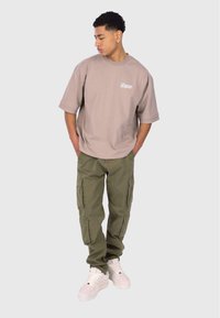 Hellbeige übergroßes T-Shirt mit Logo, kombiniert mit olivgrünen Cargo-Hosen mit Seitentaschen und weißen Sneakers.