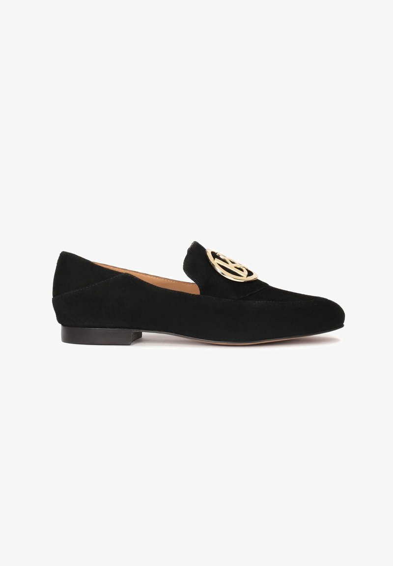 Mocassin plat en daim noir avec bout arrondi et boucle circulaire dorée sur le dessus, avec un petit talon et une doublure intérieure couleur fauve.