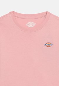 Ροζ μπλουζάκι με στρογγυλή λαιμόκοψη, με μικρό λογότυπο Dickies στο αριστερό σ τήθος και τυπωμένο όνομα της μάρκας μέσα στον γιακά.