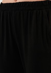 Zwarte gebreide broek heeft een elastische tailleband en zijzakken, gemaakt van zachte, lichte stof met een gladde textuur.