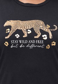 Svart T-skjorte med en leopard-silhuett i gull, omringet av gullfargede leopardprikker, med hvit tekst som sier "VÆR VILL OG FRI, men vær annerledes."