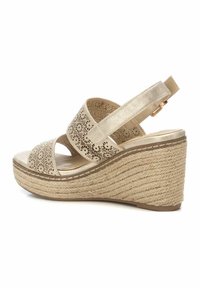 Sandalia de cuña beige con parte superior perforada, correa ajustable y suela de yute trenzado. Acabada con un brillo metálico y detalles cosidos.