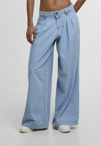 Light blue denim wide-leg jeans featuring a pleated design, front button closure, and side pockets. Smooth texture and relaxed fit.
