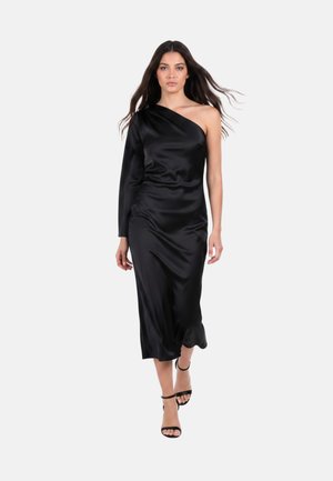 Donna che cammina in avanti indossando un abito midi in raso nero monospalla con una manica lunga e sandali neri con cinturini e tacco alto.