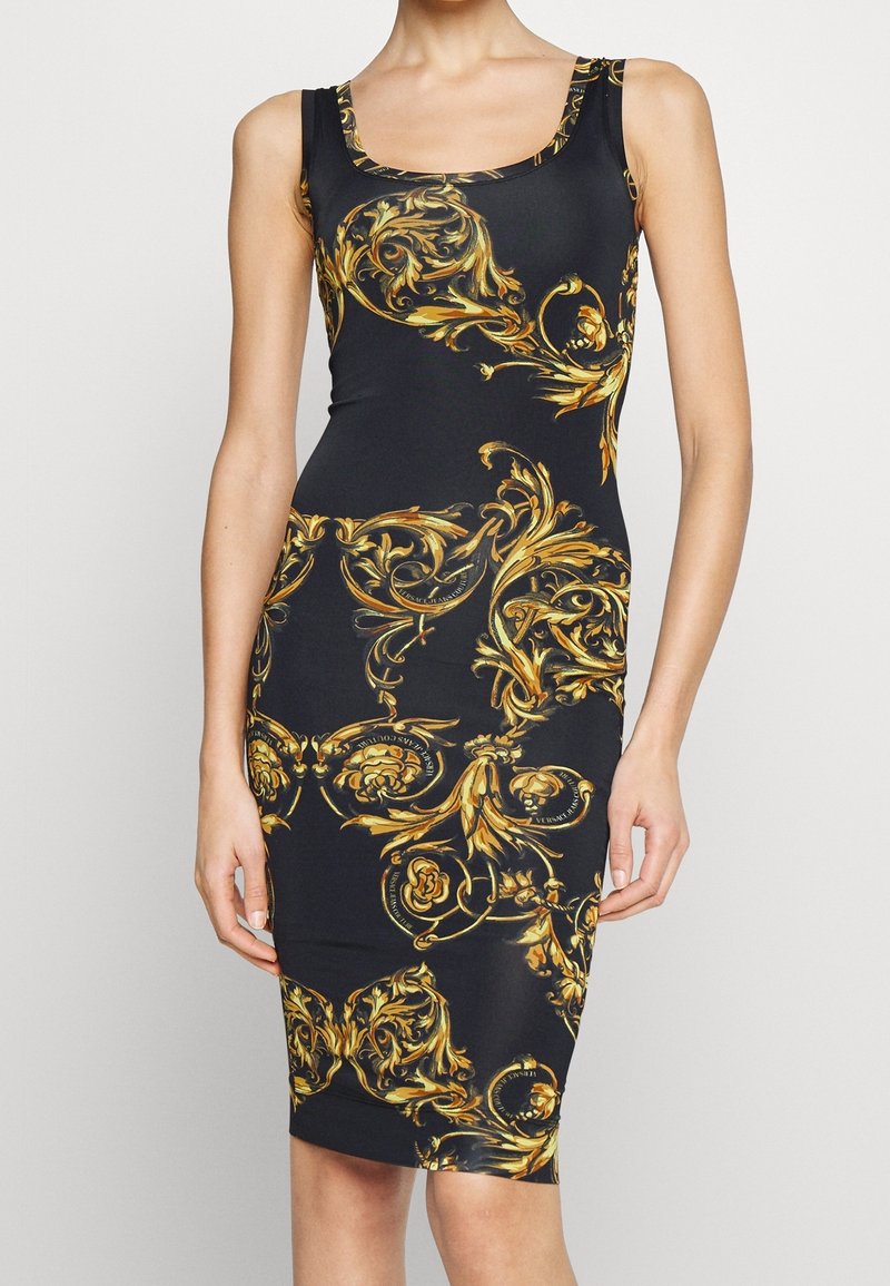 Sort ærmeløs knælængde bodycon kjole med gyldne prangende barokke blomster mønstre båret af kvinde med arme afslappet.