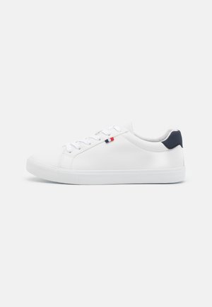 Witte lage sneaker met witte veters, een navy hielstuk en klein rood en navy vlagdetail aan de zijkant.