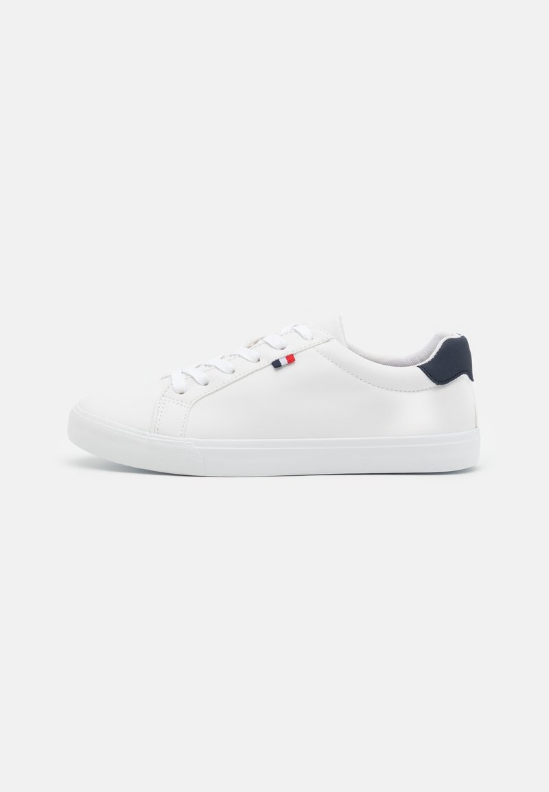 Baskets basses blanches avec lacets blancs, languette de talon bleu marine et petit détail de drapeau rouge et bleu marine sur le côté.