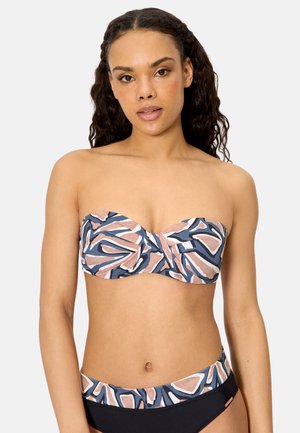 Mujer con cabello rizado, llevando un bikini sin tirantes con estampado abstracto en rosa, blanco y azul marino, y bragas de talle alto, posando frente a un fondo liso.