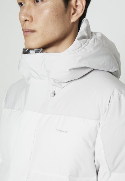 Doudoune blanche avec un col montant et une capuche ajustable. Présente un logo subtil, une texture lisse et un design matelassé pour l'isolation.