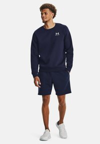 Conjunto de sudadera y pantalones cortos en color náutico, hecho de una tela suave. Sudadera con cuello redondo y logo, pantalones cortos con cintura elástica. Zapatillas blancas.