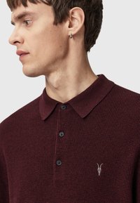 Burgundy polo shirt with a textured fabric, featuring a two-button placket, and a small embroidered logo on the chest.