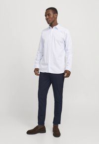 White button-up shirt with a collar, long sleeves, and a subtle texture, paired with dark navy trousers and brown shoes.