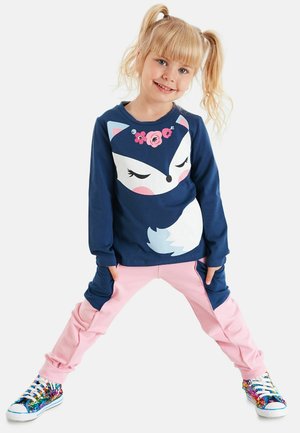 Marineblauer Sweatshirt mit einem Fuchs-Grafik und floralen Akzenten, kombiniert mit rosa Hosen mit seitlichen Taschen und mehrfarbigen, pailettenbesetzten Sneakers.