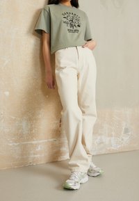 Oliivinvihreä t-paita mustalla graafisella kuvalla, kermaan sävytetyt leveälahkeiset housut ja valkoiset lenkkarit vihreillä yksityiskohdilla. Yksinkertainen, rento asu.