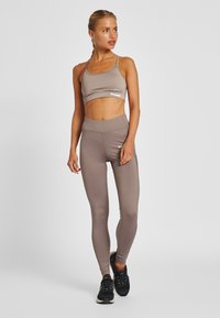 Atletische set met een lichtbruine cropped top en bijpassende high-waist leggings van gestructureerde stof met minimale branding.