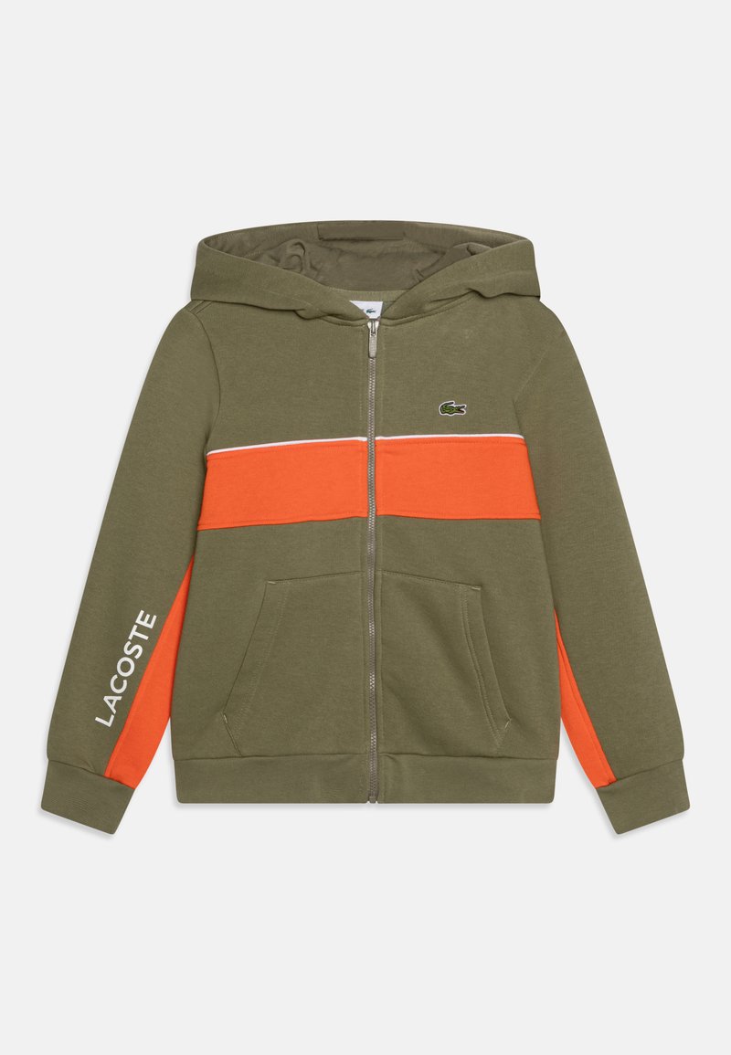 Sweat à capuche zippé vert olive avec une bande orange contrastante, comportant un accent blanc, des poches sur les côtés et le logo Lacoste sur la poitrine.