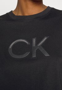 Sort bomulds T-shirt med et stort, blankt sort "CK" logo på forsiden. Rund halsudskæring med en glat tekstur.