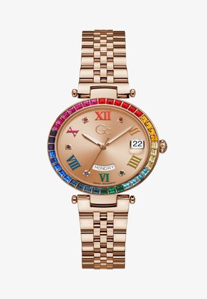 Rožu zelta pulkstenis ar dārgakmeņu rāmīti, kurā ir krāsaini akmeņi. Beigēna ciparnīca ietver romiešu ciparus un datuma displeju. Metāla saite.