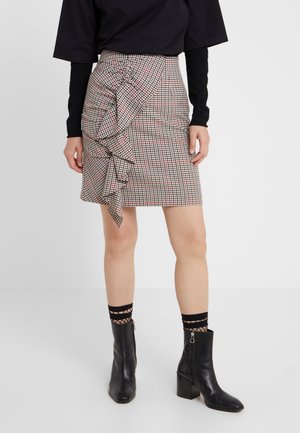 Jupe crayon à carreaux avec un détail de volants sur le côté en crème, noir et rouge, assortie à des bottines noires et des chaussettes mi-mollet.