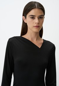Zwarte lange mouw top gemaakt van een zachte, gladde stof, met een diepe V-hals en een asymmetrisch ontwerp aan de voorkant.