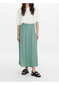 Mintgrøn maxi-nederdel med blomstermønster, elastisk talje og let stof. Sammen med en hvid oversized t-shirt og sorte sandaler.