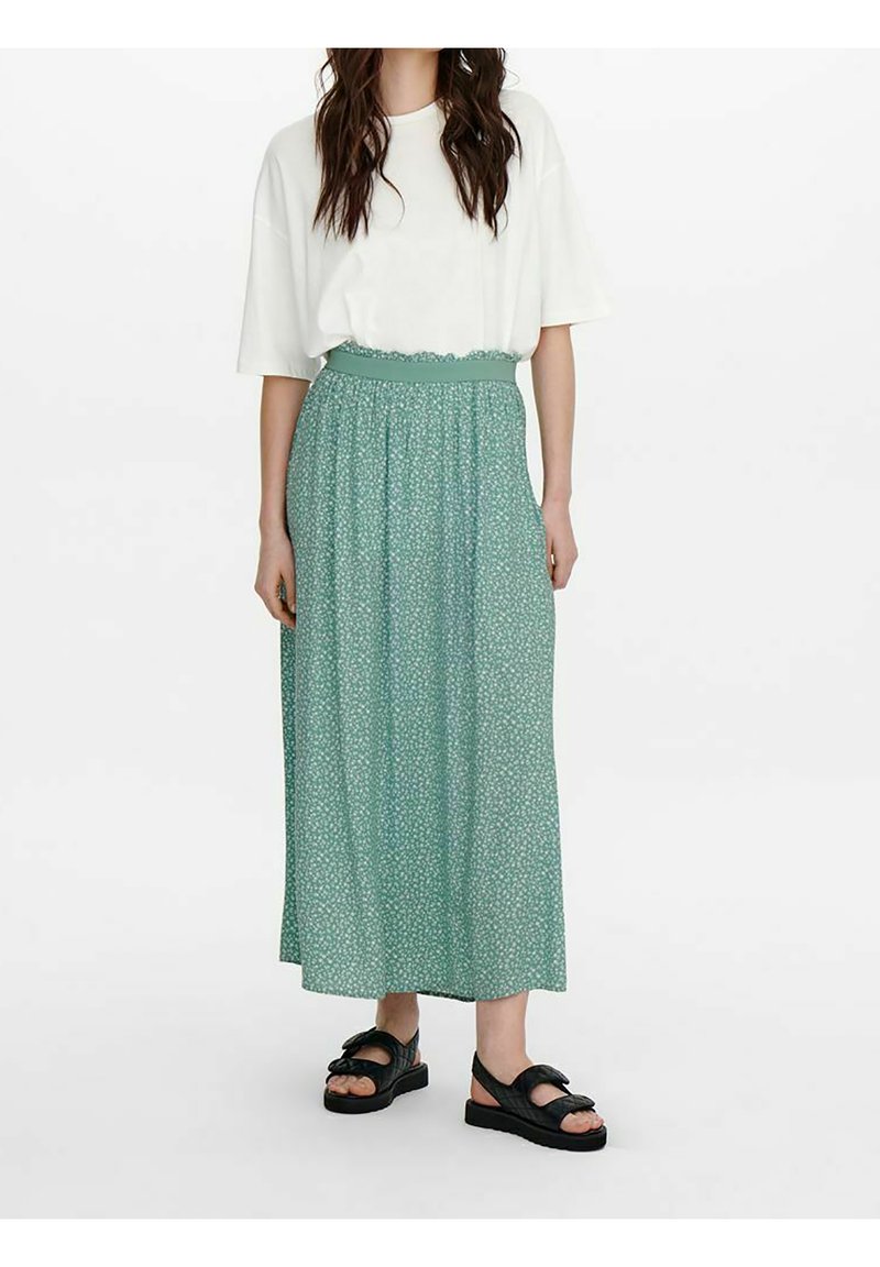 Mintgrøn maxi-nederdel med blomstermønster, elastisk talje og let stof. Sammen med en hvid oversized t-shirt og sorte sandaler.