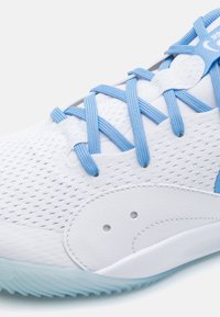 Scarpa sportiva bianca con tomaia in rete e lacci azzurri chiari. Presenta dettagli cuciti e una suola in gomma testurizzata. Design della punta arrotondata.
